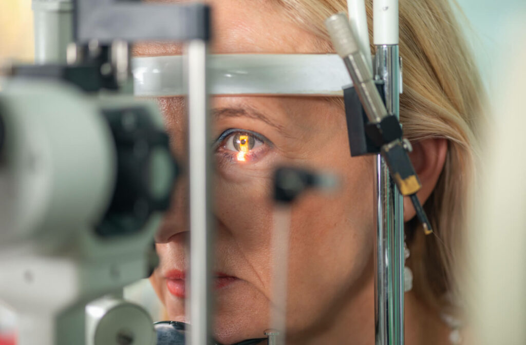 A woman standing in front of a slit lamp during her eye exam to check for glaucoma.