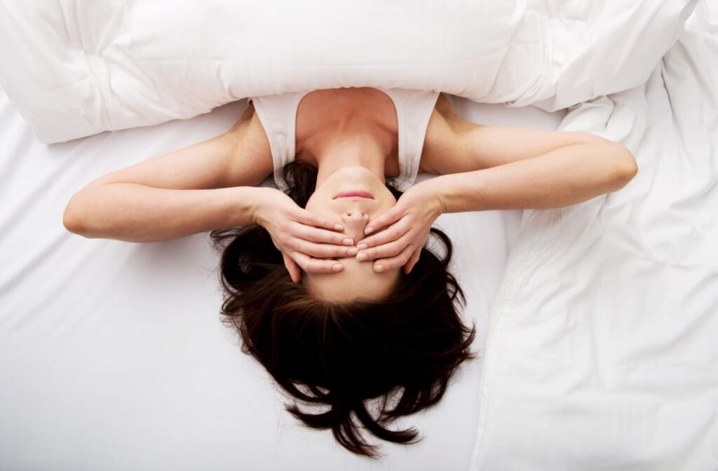 Overhead view of a woman waking up in bed covering her dry eyes in the morning