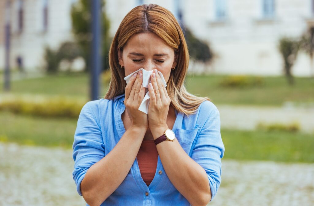 A person blowing their nose outside due to seasonal allergies