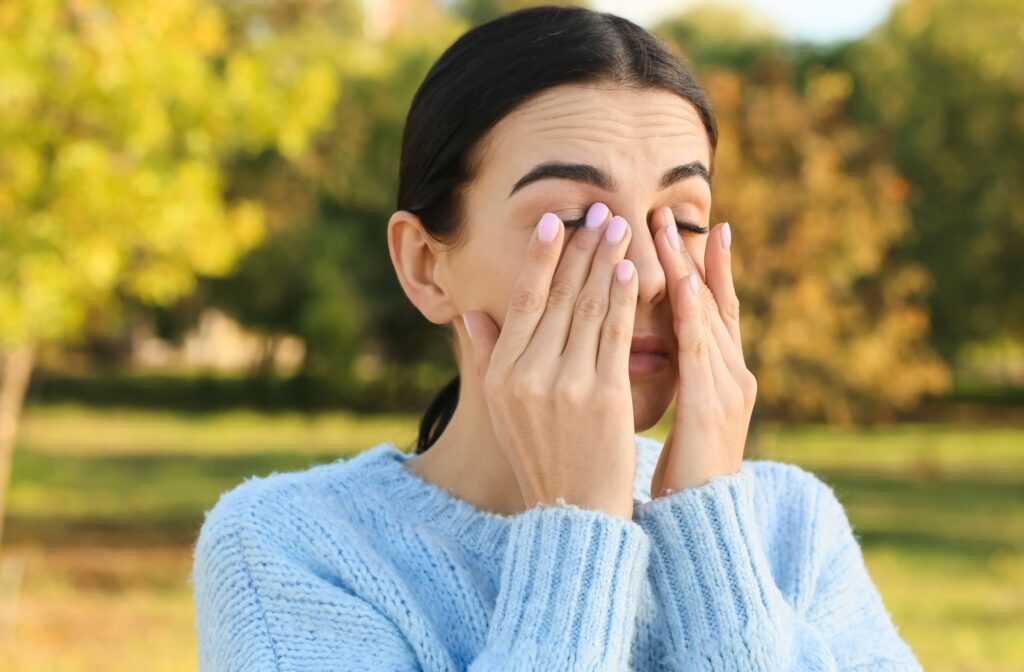 A person standing outside and rubbing their irritated eyes